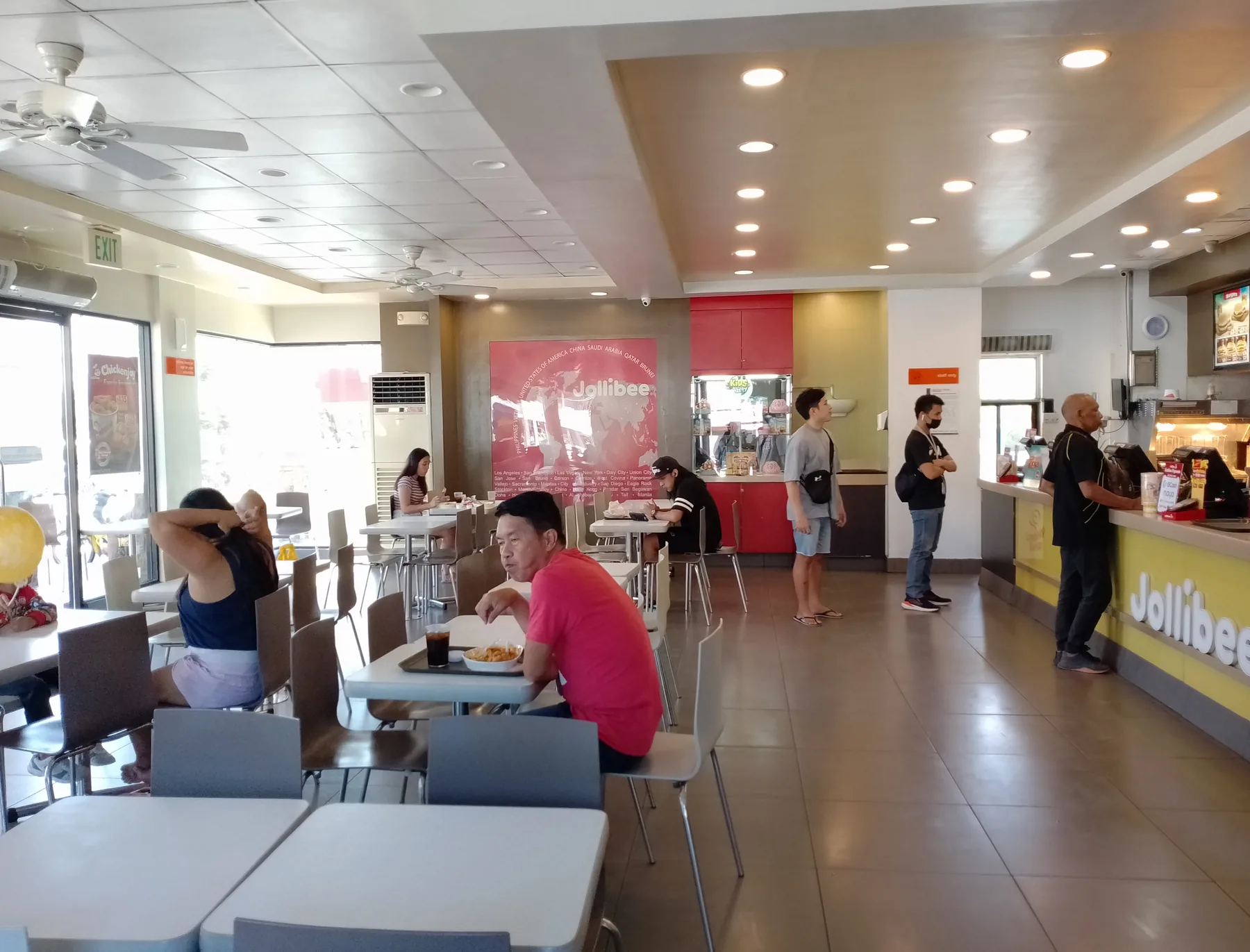 A Jollibee dining room with rows of tables, ceiling fans and a service counter at the far end