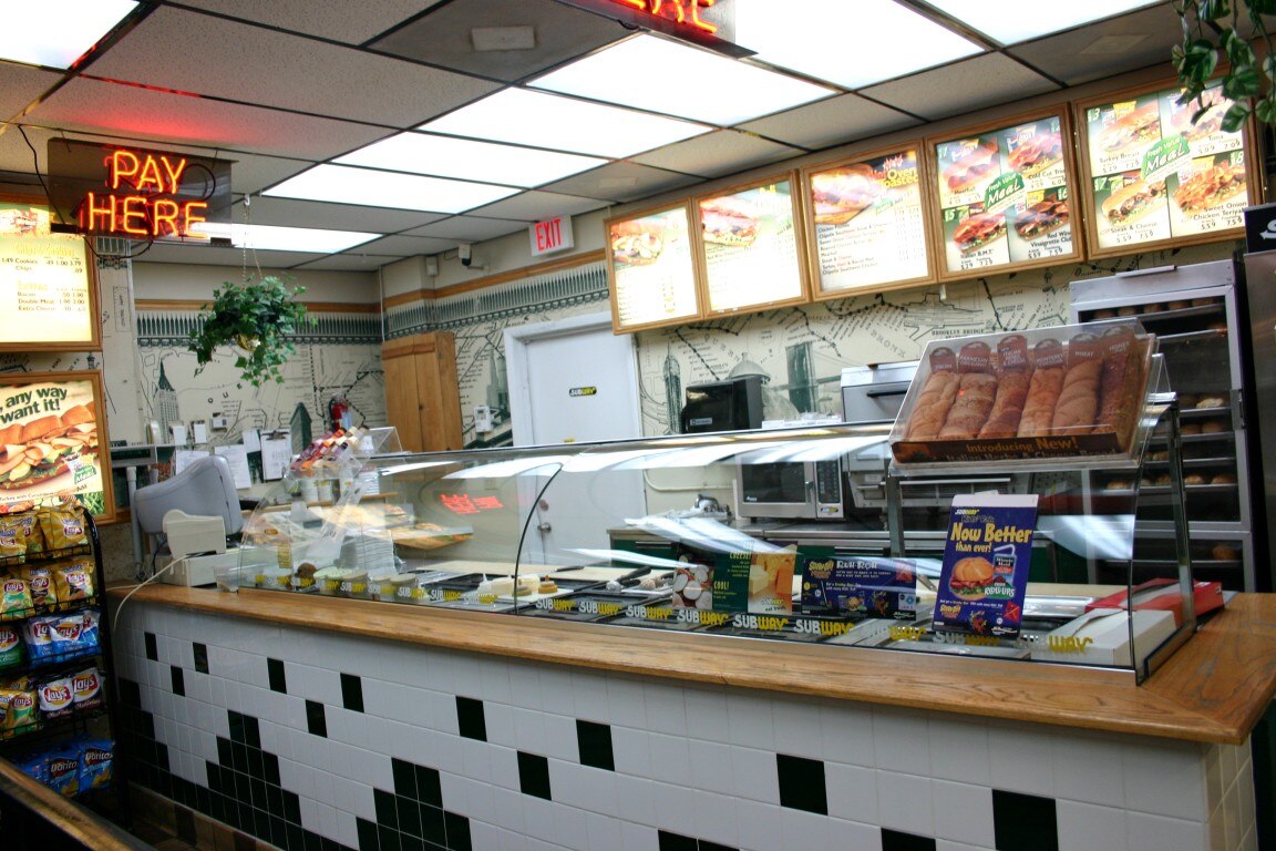 A Subway counter with ingredients displayed behind glass along an assembly line